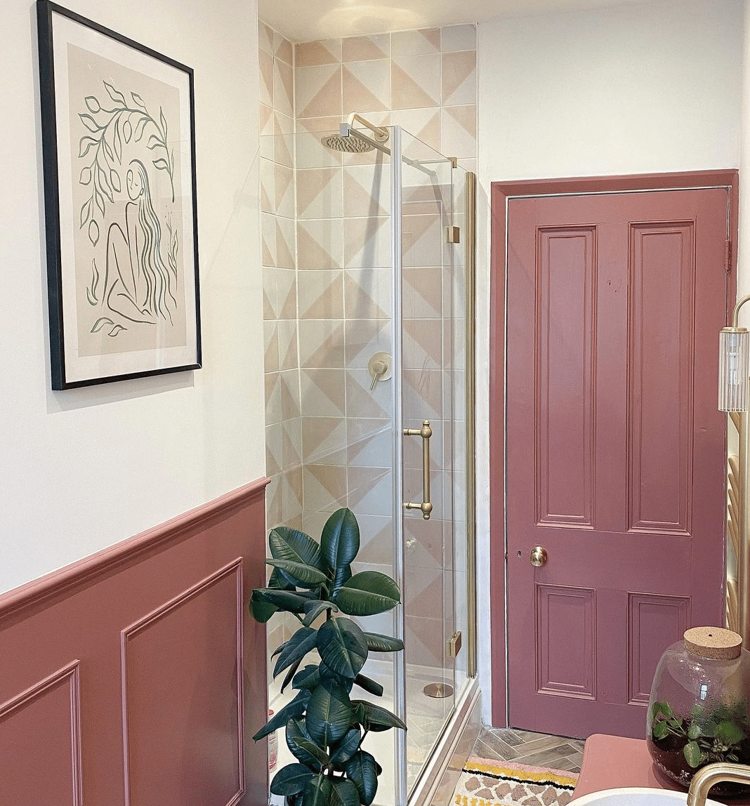 bold pink bathroom half wall paneling with matching pink door and shower enclosure with pink and white tiles and brass hardware details