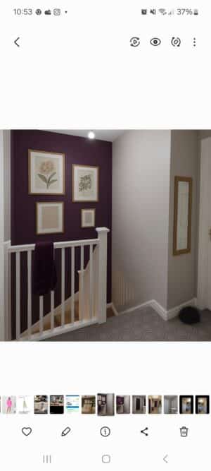 A cozy hallway with deep plum and soft beige walls, featuring white railing, botanical prints in wooden frames, and geometric tile flooring. A plum towel hangs over the banister, and a full-length mirror leans on the beige wall.