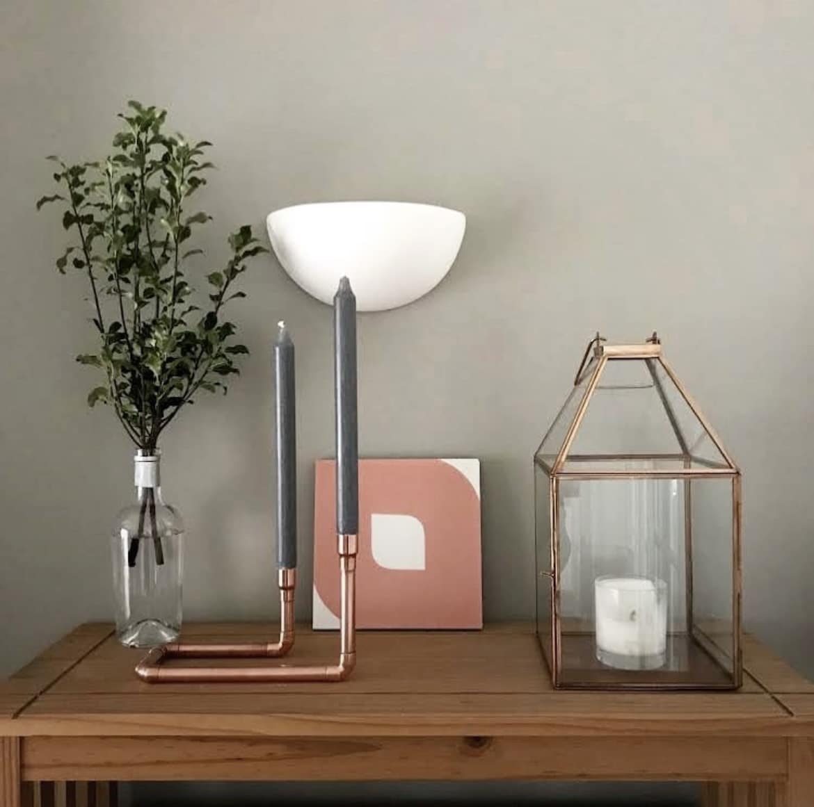 copper candlestick holders and lantern sat on a wooden console table against a green wall