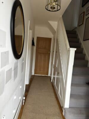 A hallway with a long rug leading to a wooden door, showing a staircase and a large mirror on the wall.